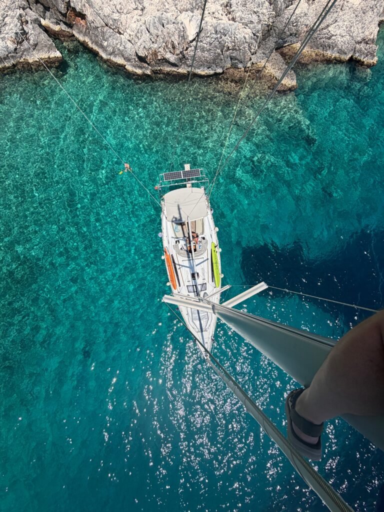 Sailing yacht anchored in clear turquoise water beside a rocky Ionian coastline
